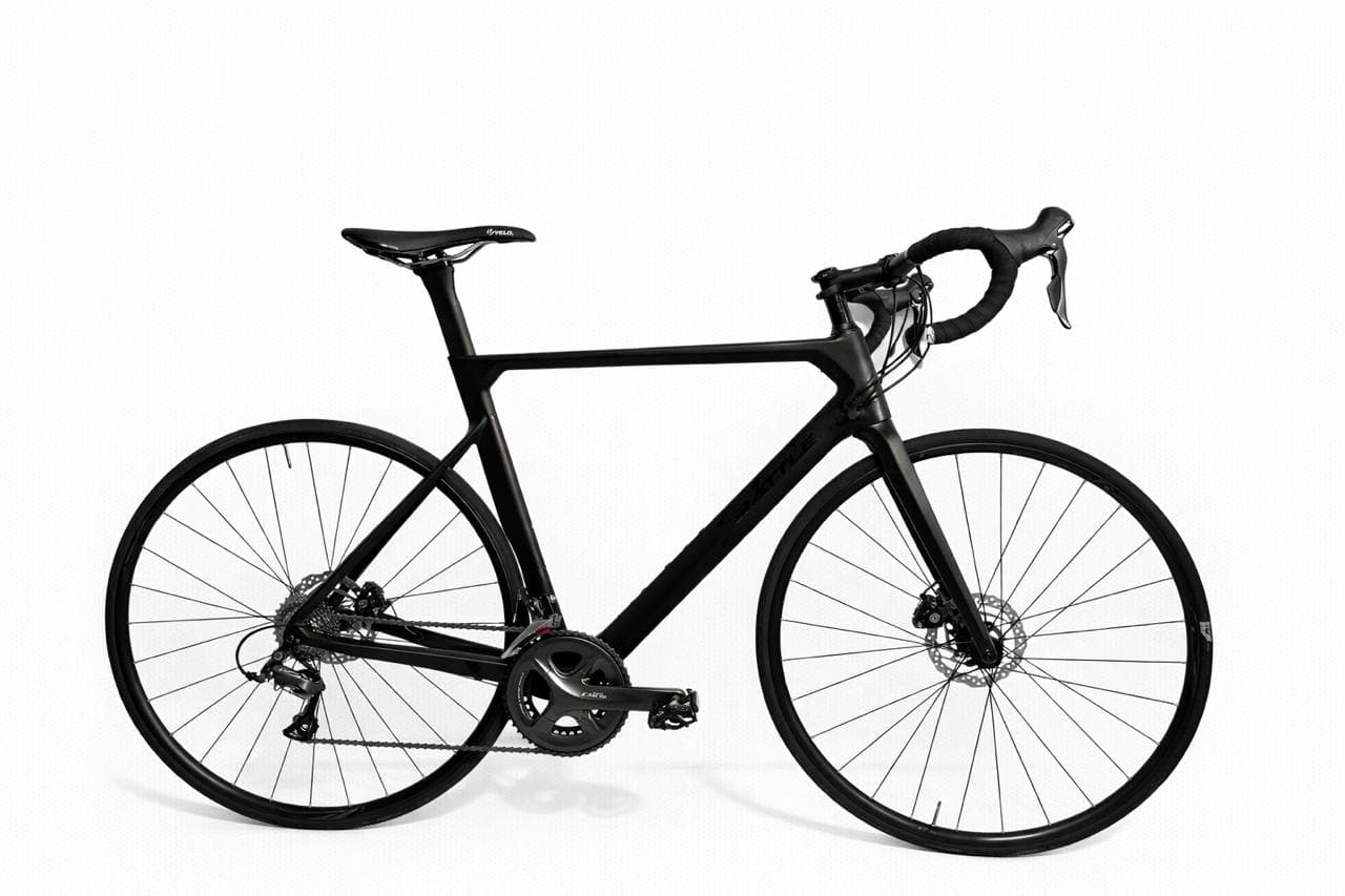 Bicicleta de carretera negra mate con cuadro de carbono y frenos de disco sobre blanco.